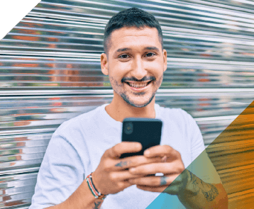A smiling man in a white t-shirt looks up from his phone as us